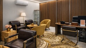 A modern hotel room with leather chairs, a round table, a desk with a computer, a lamp, and a decorative rug. - Hotel Zenite (Angra do Heroismo)