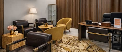 Una habitación de hotel moderna con sillones de cuero, una mesa redonda, un escritorio con una computadora, una lámpara y una alfombra decorativa.