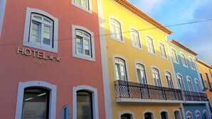 A hotel with a pink facade, yellow and blue upper floors, and a balcony with a wrought iron railing. - Hotel Zenite (Angra do Heroismo)