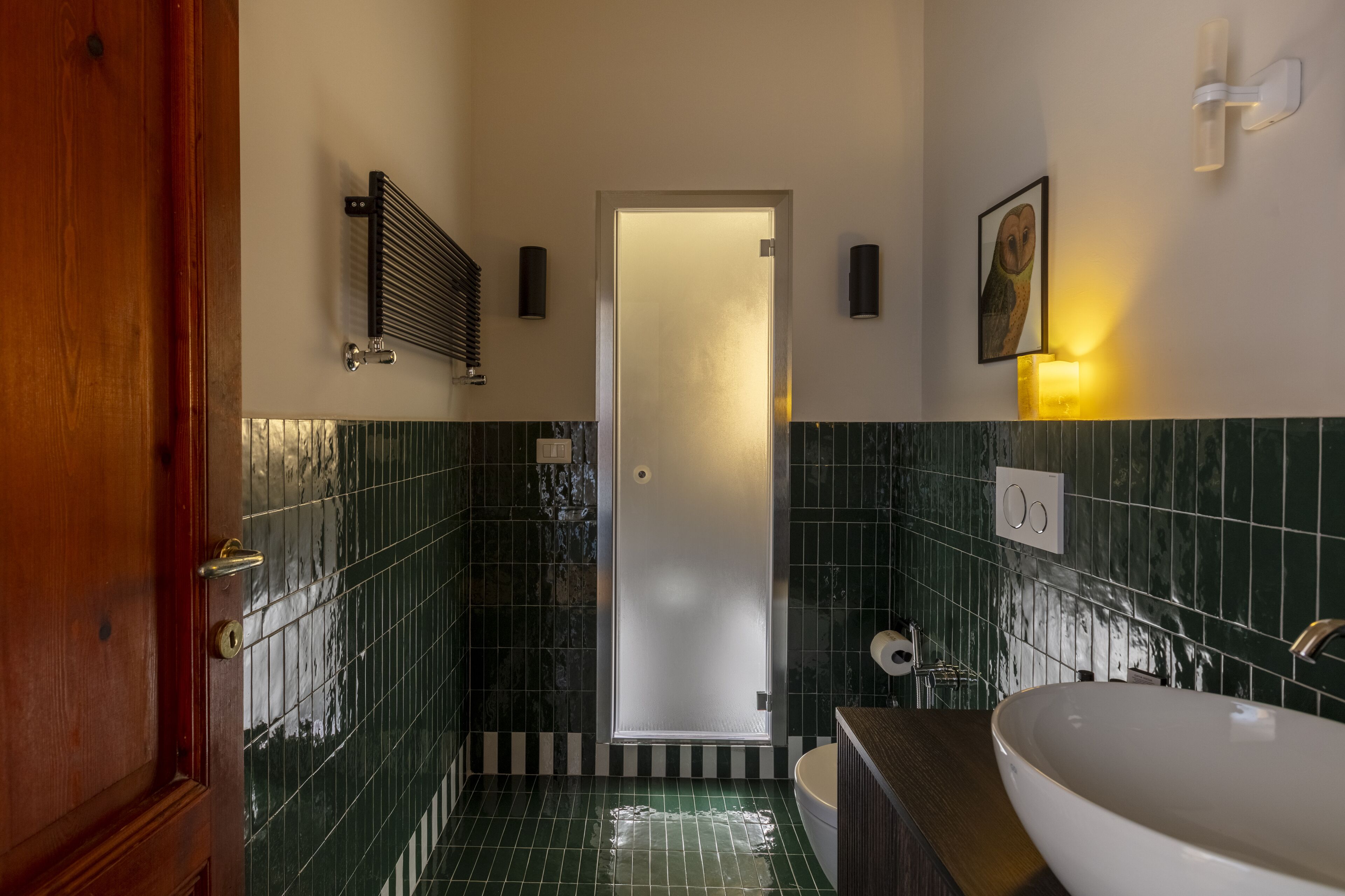 A bathroom with a large sink, a shower, and a toilet. There is a wooden door and a towel rack.