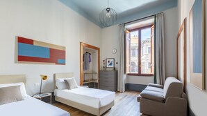 Habitación de hotel con dos camas, un sofá, un escritorio y un ventanal con vistas a la ciudad.