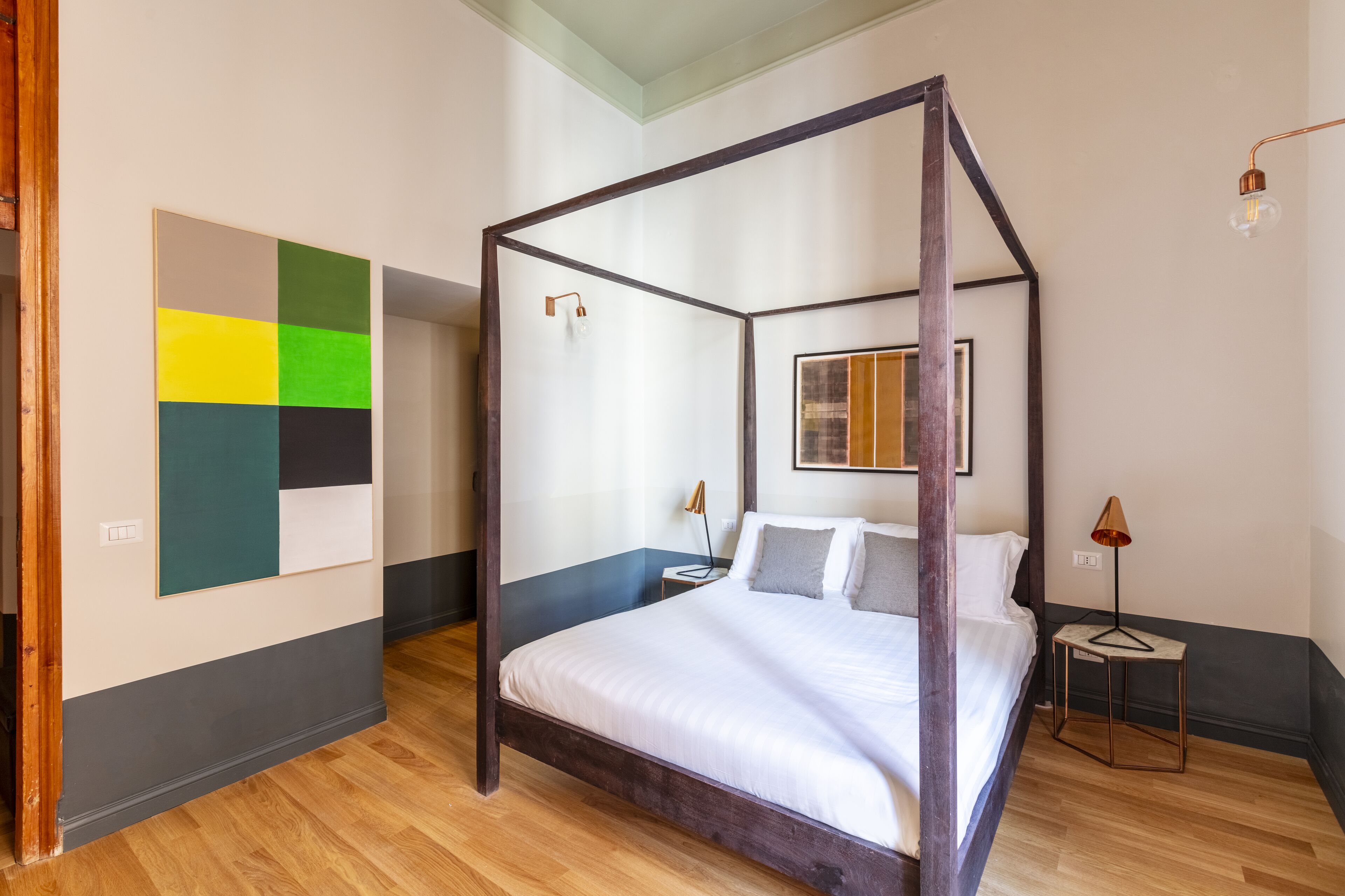 A four-poster bed with a wooden frame, a bedside table with a lamp, and a wall art piece.