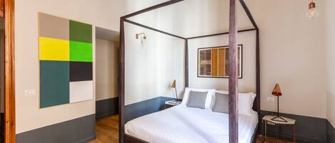 A four-poster bed with a wooden frame, a bedside table with a lamp, and a wall art piece.