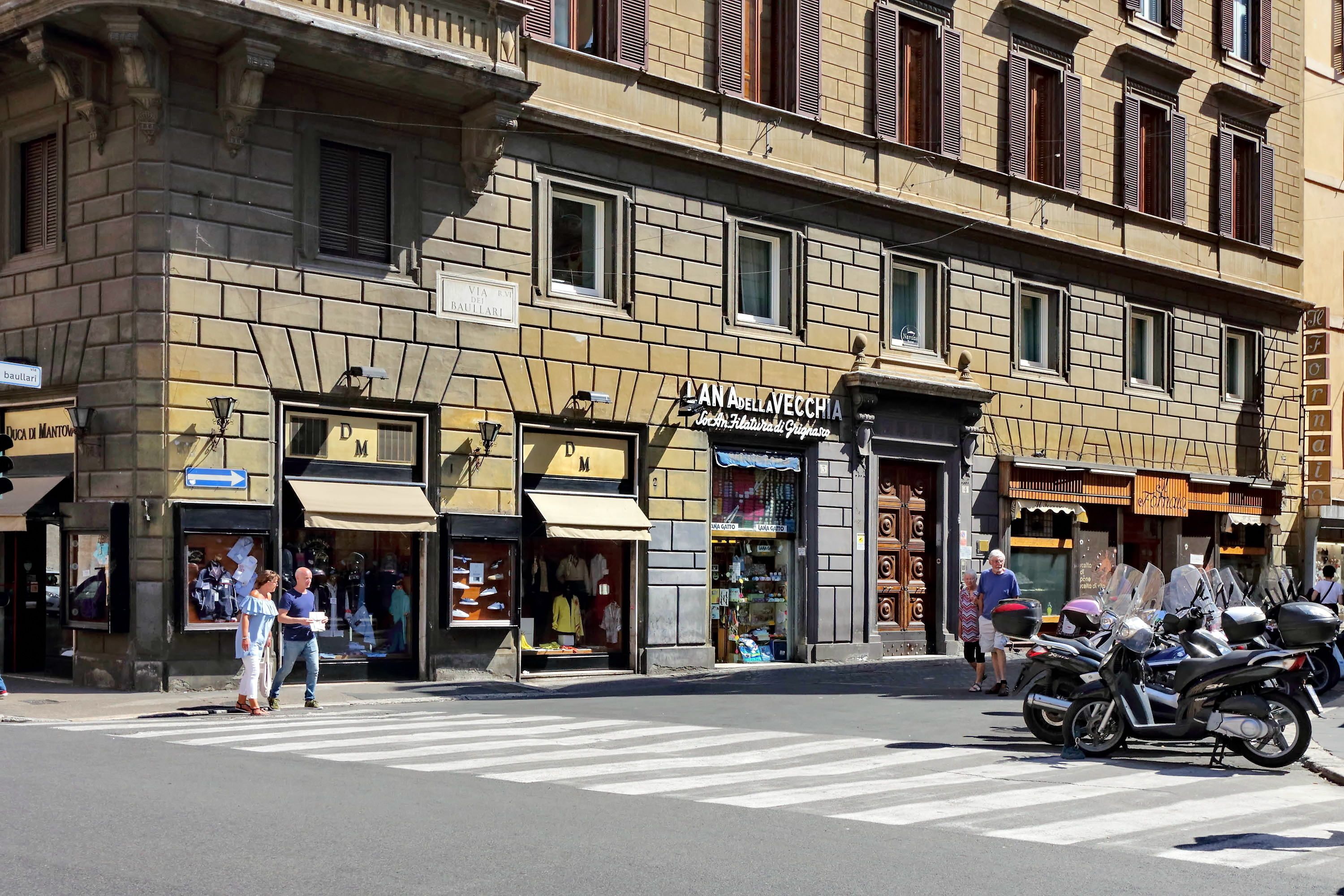 A street view with a building featuring a shop named "AN APOLLEA VECCHIA" and another shop with a sign "D M".