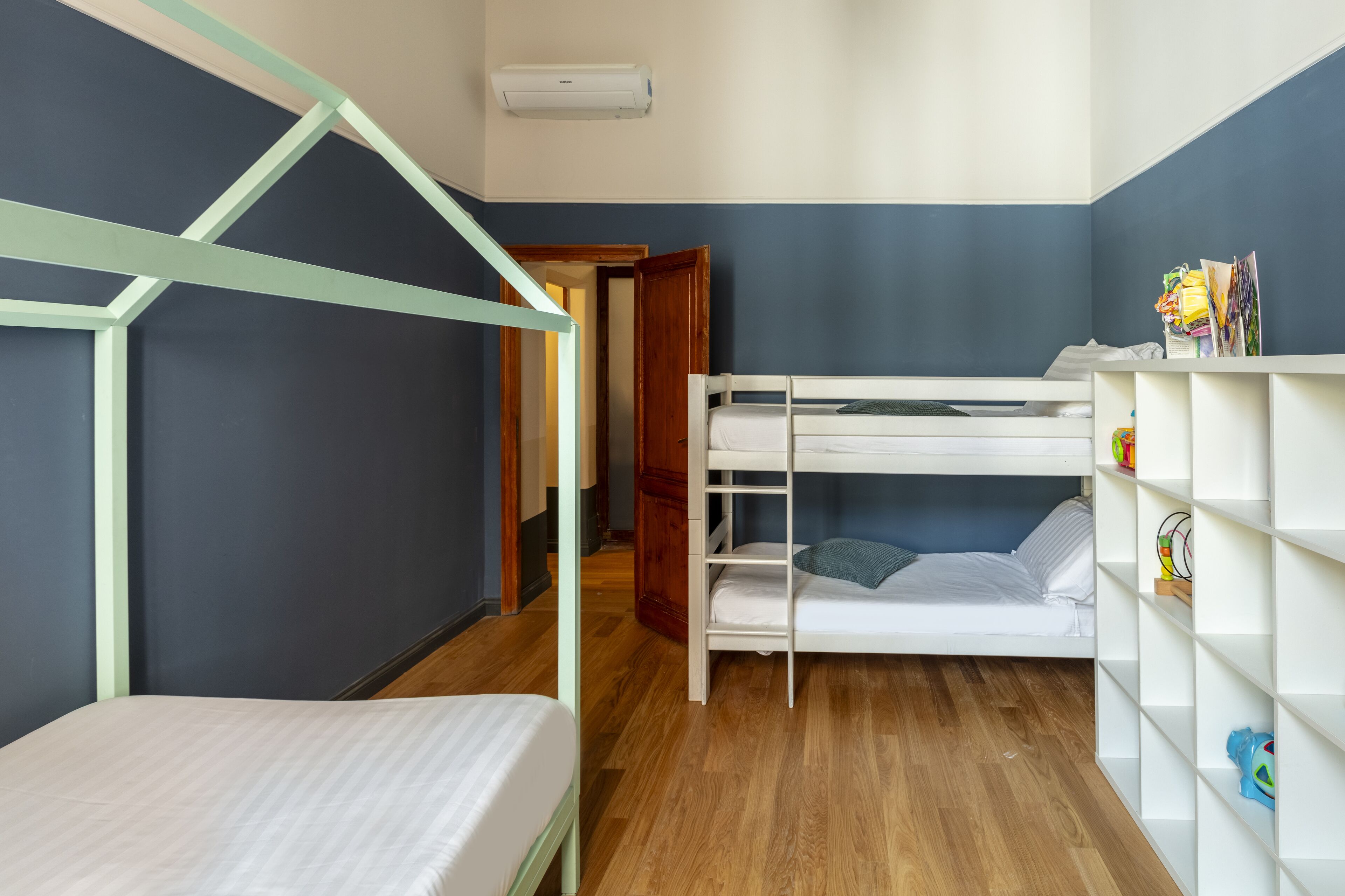 A room with a bunk bed, a small desk, and a bookshelf.