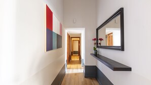 Un pasillo con suelo de madera, un estante negro flotante con un florero y un espejo grande en la pared.