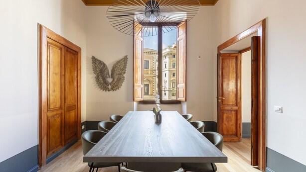 Un comedor con una mesa larga, sillas, un florero y un adorno decorativo con forma de ala.
