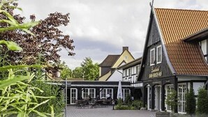 Een traditioneel vakwerkhuis met pannendak, een naambord en een terras.