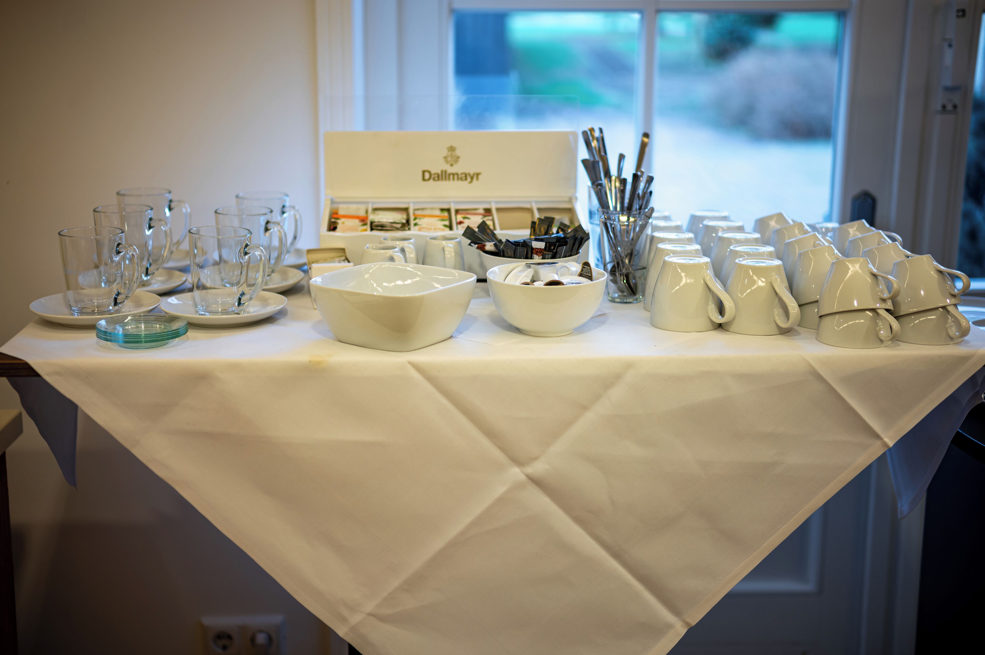 A table with various glassware and bowls, a sign reading "Dallmayr," and a window in the background.
