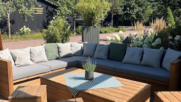 A wooden outdoor seating area with a sofa and ottomans, a checkered tablecloth, and a potted plant.