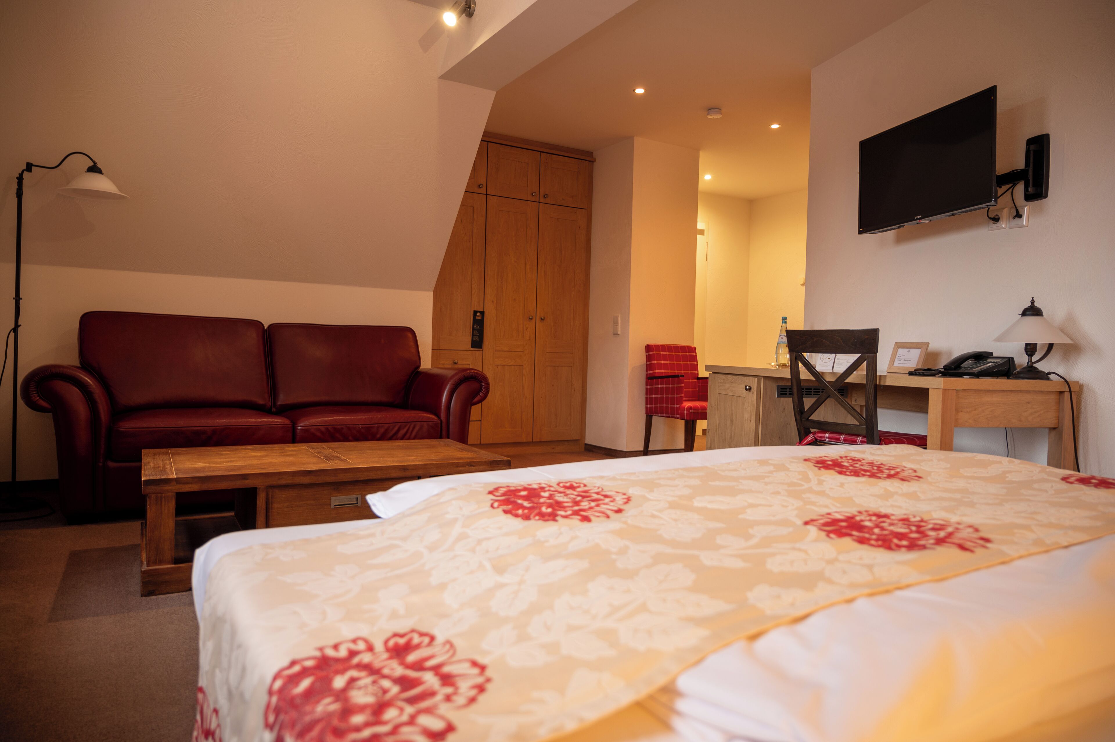 Una habitación de hotel con cama, sofá de cuero rojo, escritorio de madera, silla, televisor y armario.