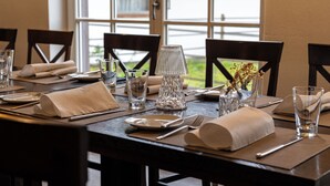 Een eettafel gedekt met borden, bestek, glazen en servetten, omringd door stoelen.