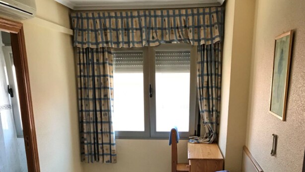 A room with two beds, a desk, and a window with curtains.