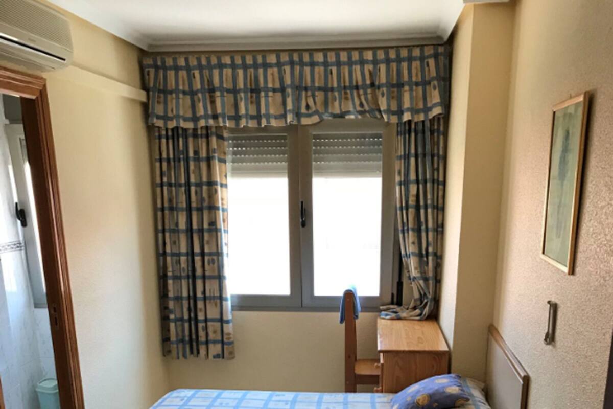 A room with two beds, a desk, and a window with curtains.