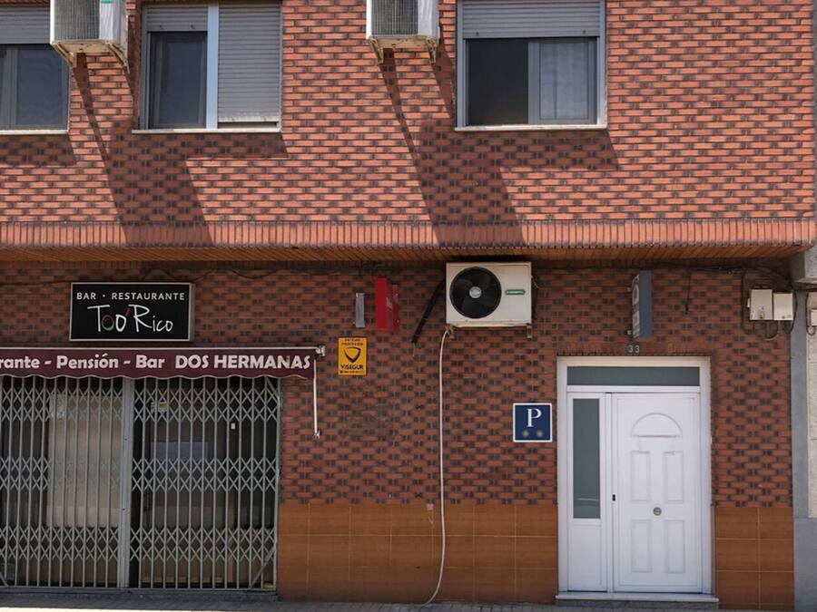 A brick building with two air conditioning units, a sign for 'Bar Restaurante Too Rico', and a 'P' parking sign.