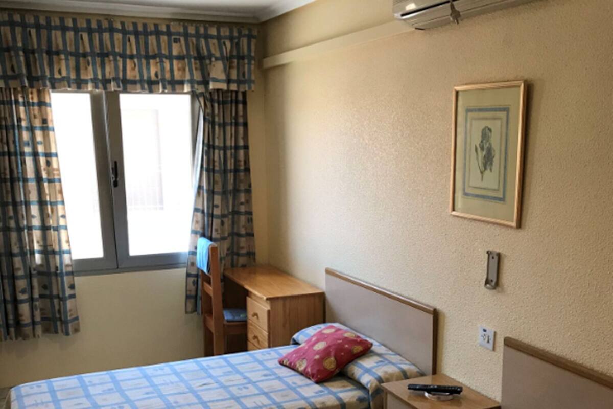 A bedroom with two beds, a desk, and an air conditioning unit.