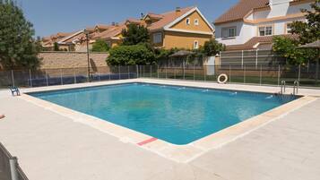 Una piscina rectangular con un borde de baldosas, rodeada por una cerca y un muro de piedra.