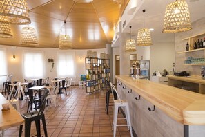 L’intérieur d’un restaurant avec un plafond en bois, des lampes en osier suspendues, des chaises blanches et un coin bar.
