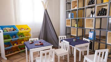 Zona de juegos infantiles con mesas, sillas y contenedores.