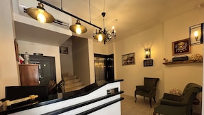 Un área de recepción con mostrador blanco y negro, una escalera, un sillón verde y un candelabro.