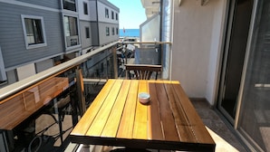Un balcón con mesa y sillas de madera, con vistas a una zona costera con edificios y cielo despejado.