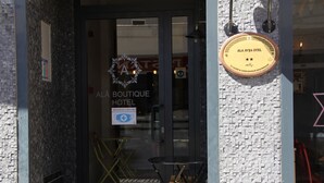 La entrada a ALA BOUTIQUE HOTEL con una puerta de vidrio, una placa en la pared y un letrero que indica el uso de mascarilla.