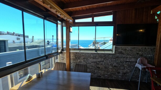 Una habitación con un ventanal grande con vista al mar, una mesa de madera y un televisor montado en la pared.