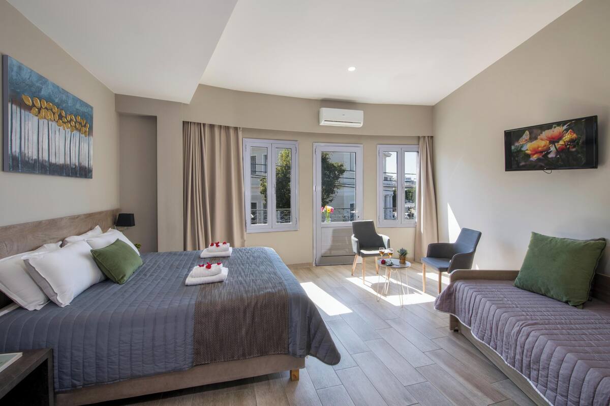 A modern hotel room with a large bed, two smaller beds, a balcony with a chair, and artwork on the walls.