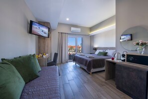 A modern hotel room with a sofa, a bed, a desk, a TV, and a view of the outdoors. - Stoa Suites Chania (Chania)