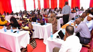 Une salle de conférence avec des tables rondes, des participants assis et un orateur à l’avant de la salle.