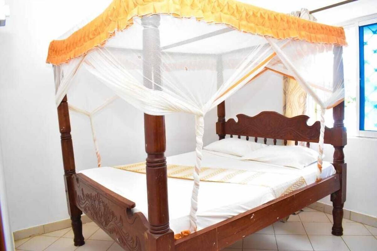 A four-poster bed with a canopy, wooden frame, and white bedding.