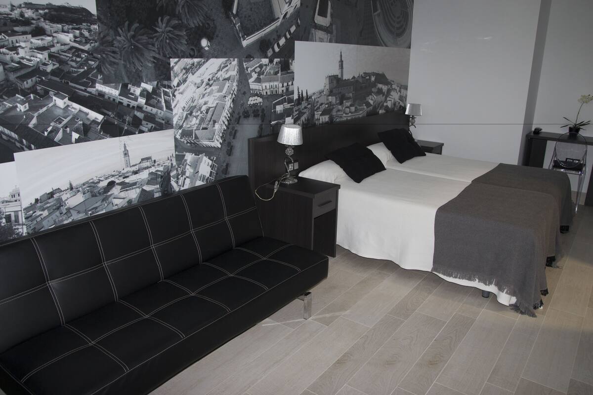 Un dormitorio moderno con una cama grande, un sofá negro y una mesita de noche con una lámpara.