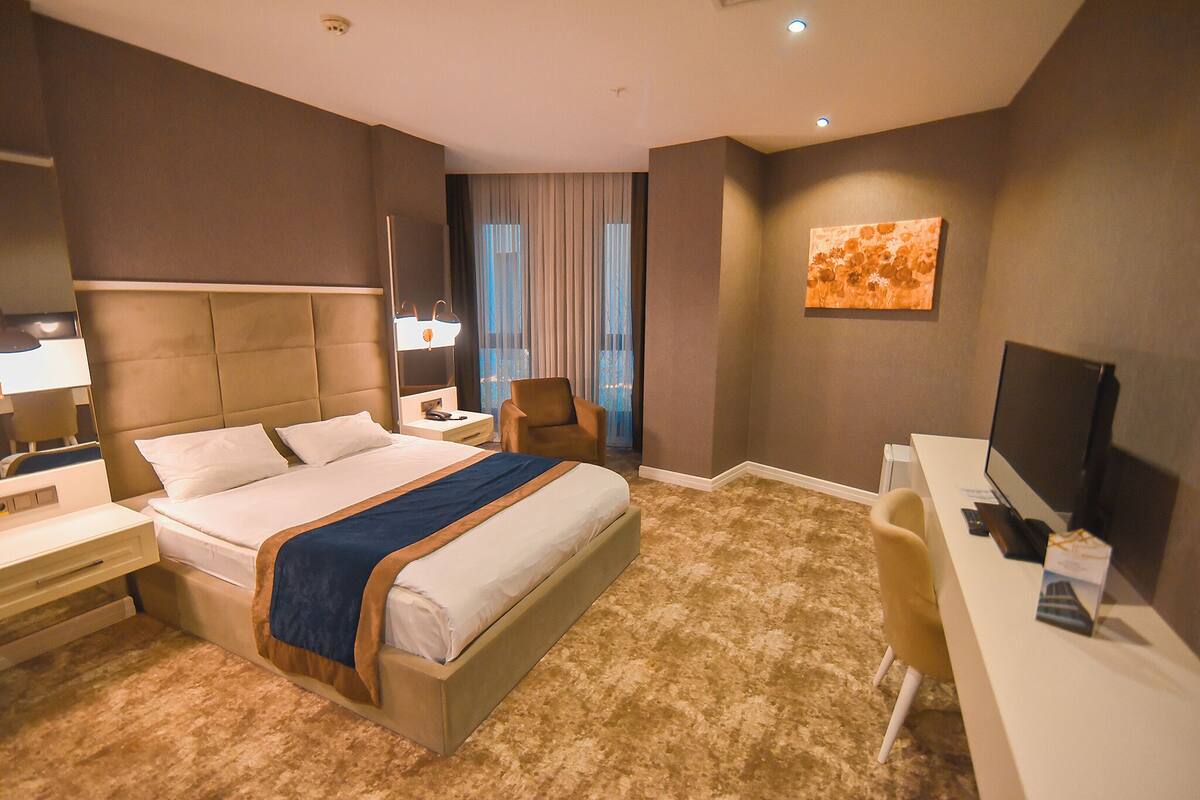 A hotel room with a large bed, a desk, a chair, a television, and a window with curtains.