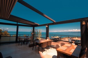 A terrace with tables and chairs overlooking a scenic ocean view. - Royal Comfort Hotel (Arakli)