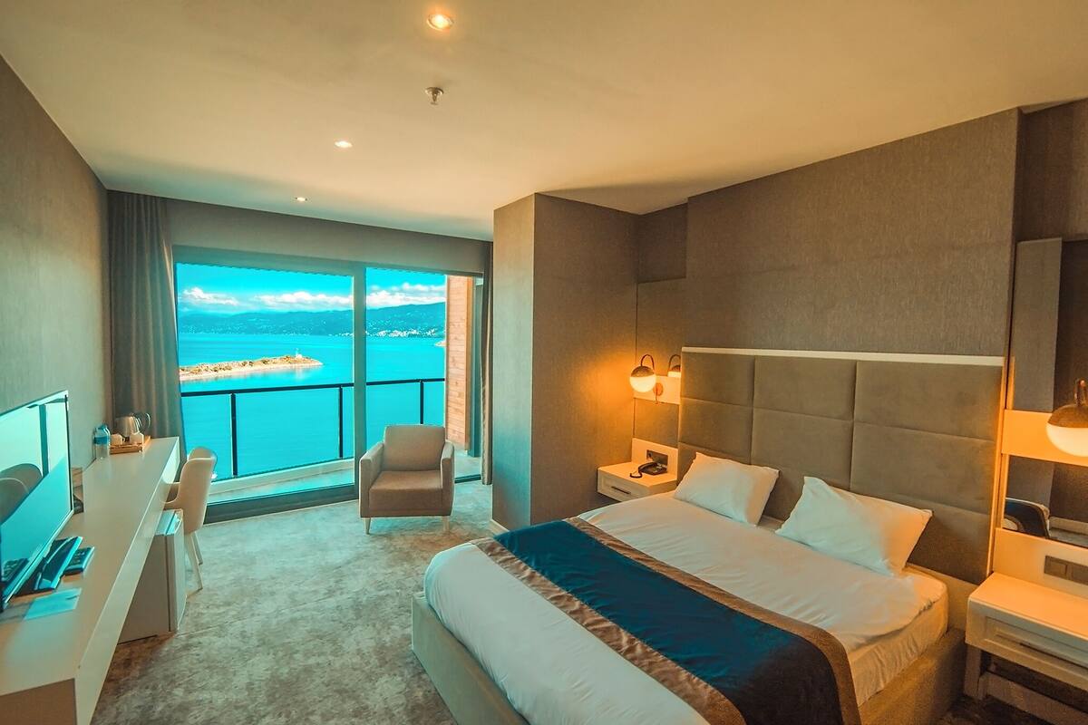 A hotel room with a large bed, a desk, a chair, and a view of the sea.