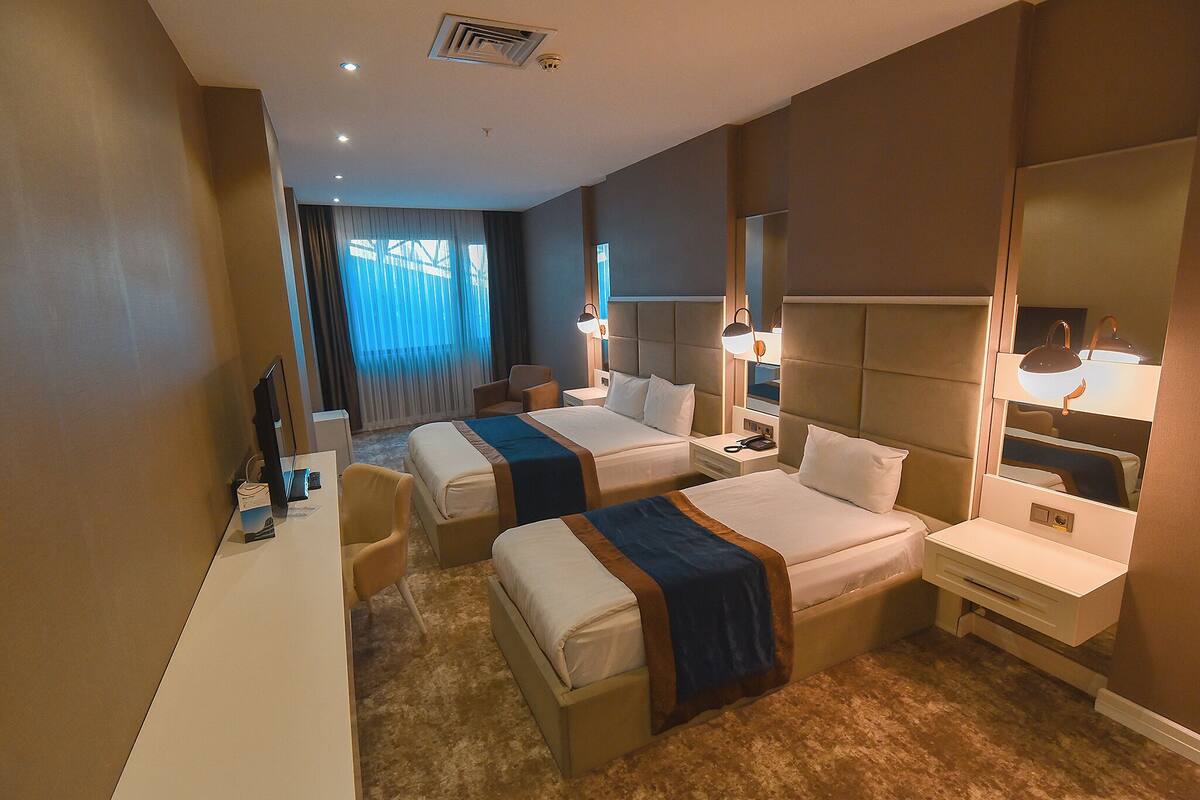 A hotel room with two beds, a desk, and a mirror.