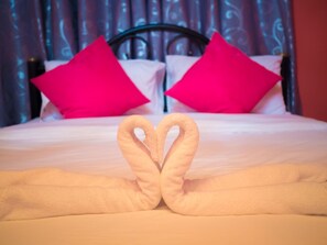Una cama con dos almohadas rosa brillante y una toalla dispuesta en forma de corazón.