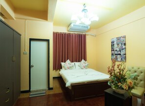 Une chambre d’hôtel avec un lit, une table de chevet, une chaise, un climatiseur fixé au mur, une porte et une affiche accrochée au mur.