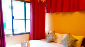 A neatly made bed with white bedding and decorative pillows, a window with red curtains, and a warm yellow wall. - De Sky Sukhumvit Ekkamai (Bangkok)