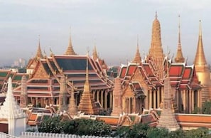 Un complexe de temples traditionnels thaïlandais comprenant plusieurs bâtiments, dont des flèches richement décorées et un bâtiment central surmonté d’un toit rouge et doré.