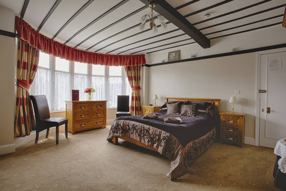 A bedroom with a large bed, wooden dresser, chair, and a nightstand with a lamp.
