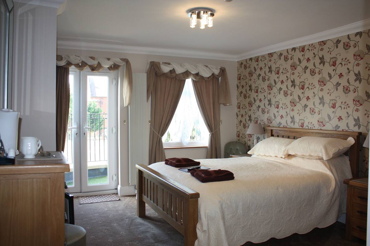 A bedroom with a wooden bed, a bedside table, a chair, and a window with curtains.