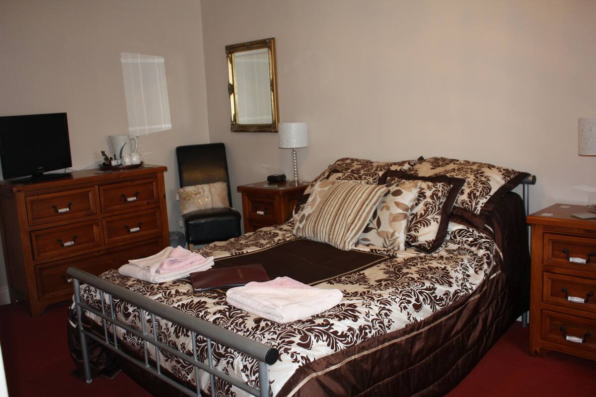 A bedroom with a bed, a dresser, a nightstand, a lamp, a television, and a mirror.