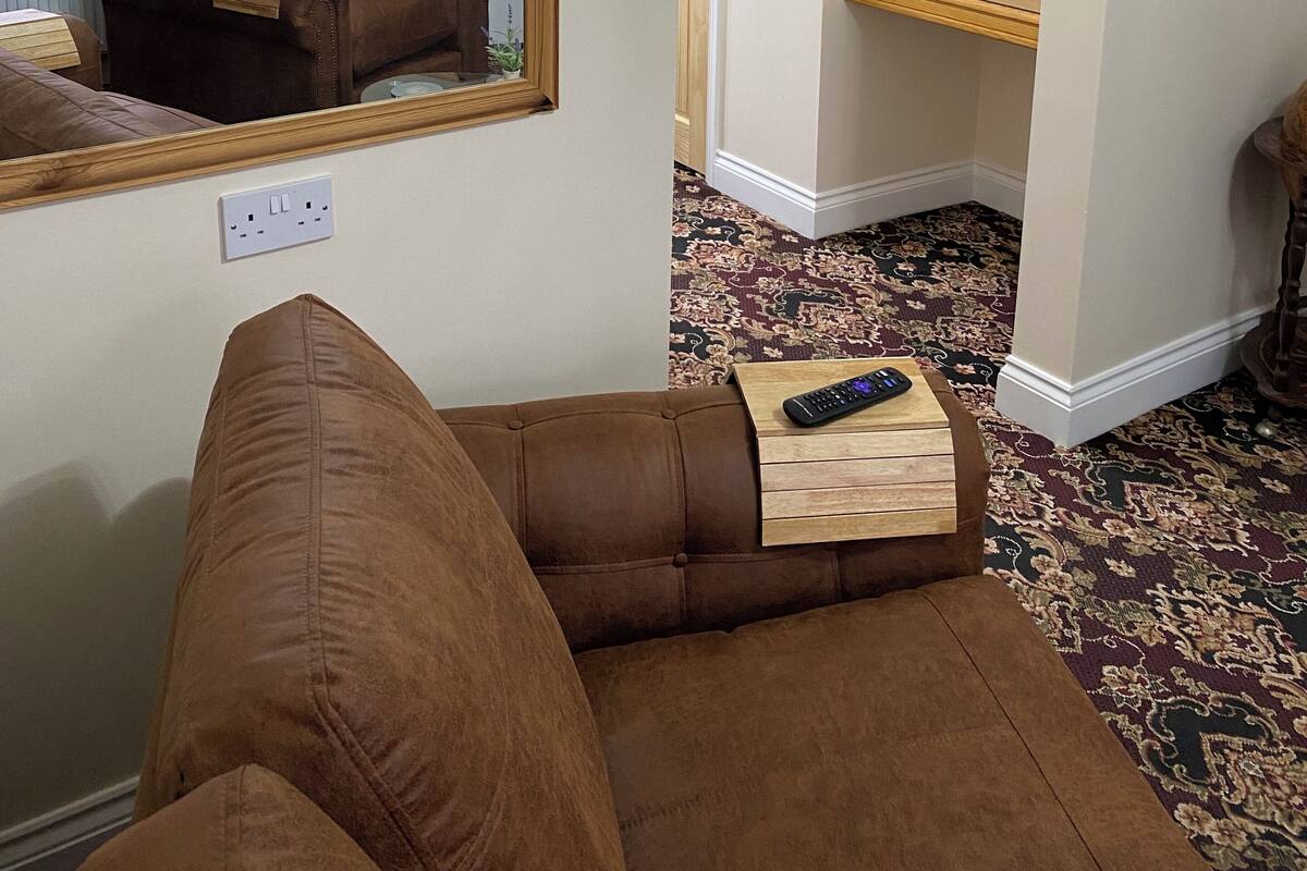 A room with a brown leather sofa, a wooden side table, a mirror, and a shower area with a wooden bench.