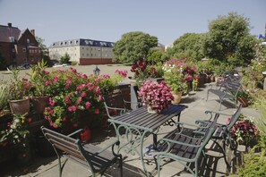 Een terras met banken en tafels, omringd door potplanten en bloemen.