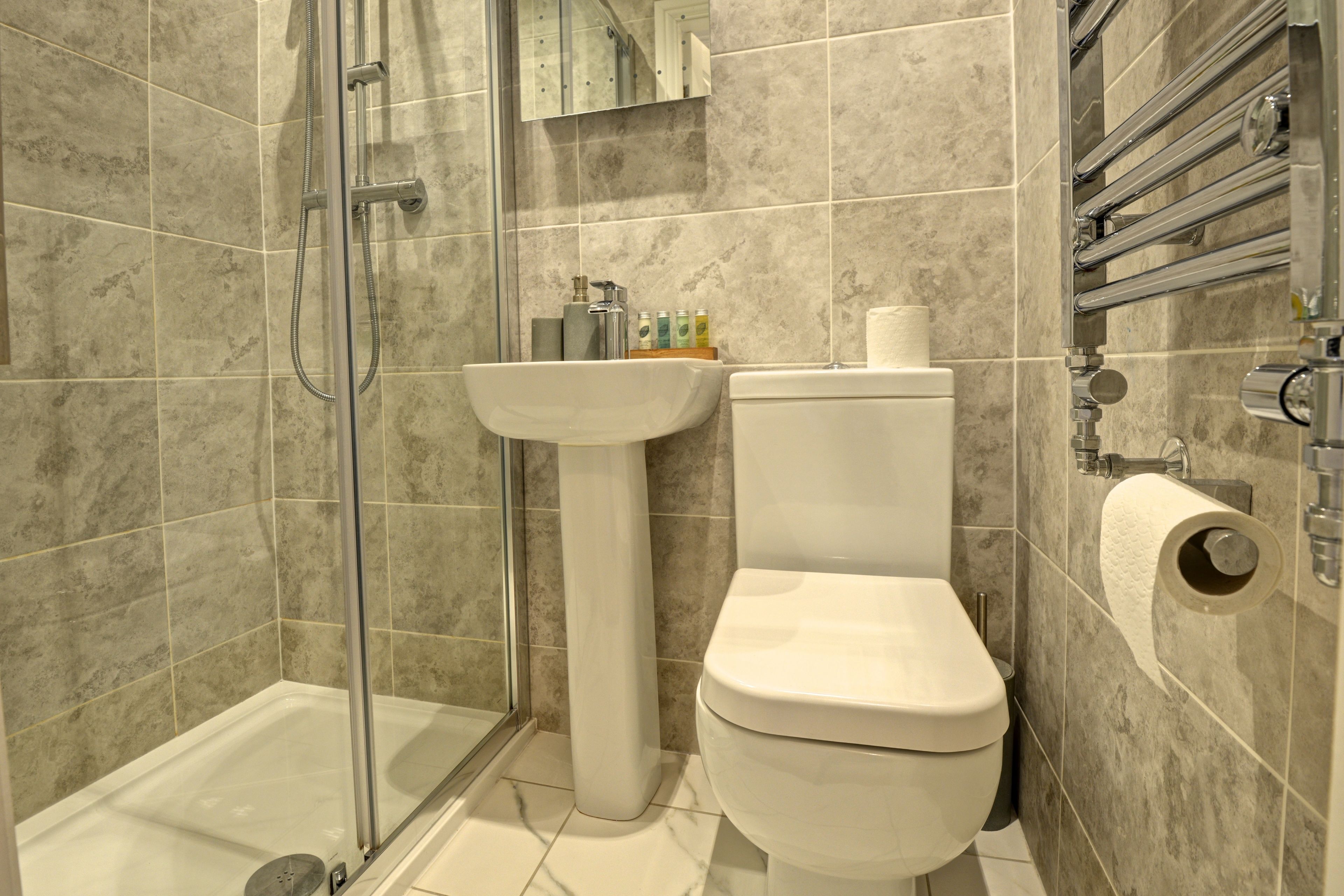 A bathroom with a glass shower enclosure, a pedestal sink, and a toilet.