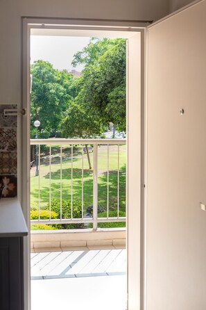 An open door to a balcony with a view of a well-maintained garden and trees. - Sea View Suite (Hof HaCarmel)
