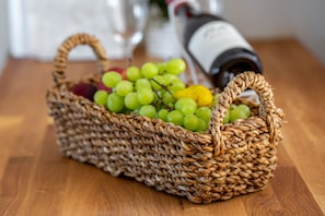A wicker basket filled with green grapes and a bottle of wine on a wooden table. - Sea View Suite (Hof HaCarmel)