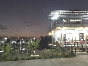 Un edificio con fachada de vidrio, un balcón y una fuente de agua reflectante al frente.