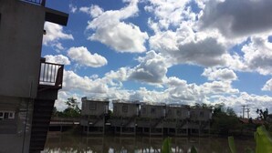 Blick auf einen Fluss mit einer Reihe von Gebäuden, einige mit Balkonen, unter einer teils bewölkten Himmel.